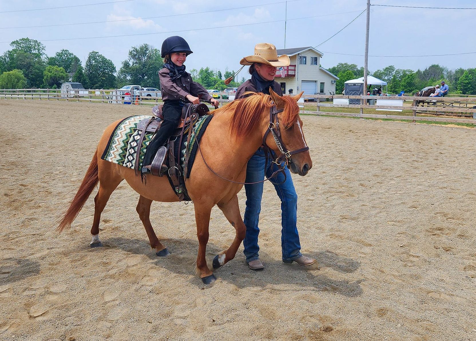 Little girl with big smile riding a horse with a guide