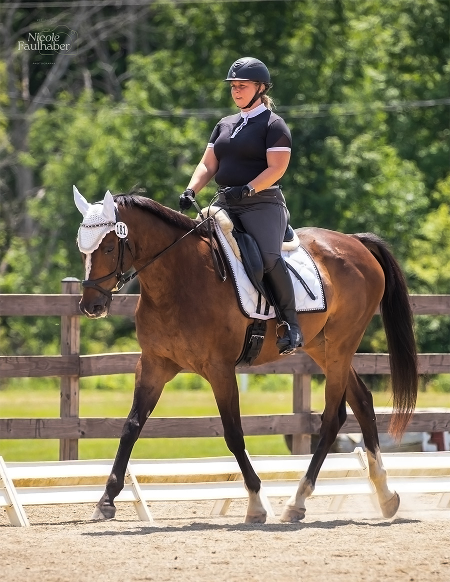 Women riding dark brown horse that is wearing a white ear cover