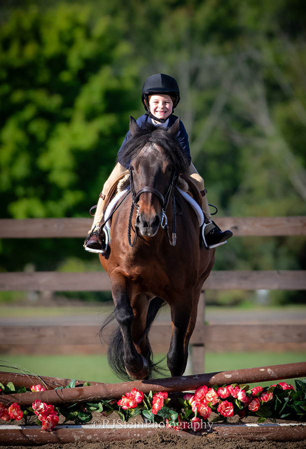 Little kid smiling at the camera while riding a horse