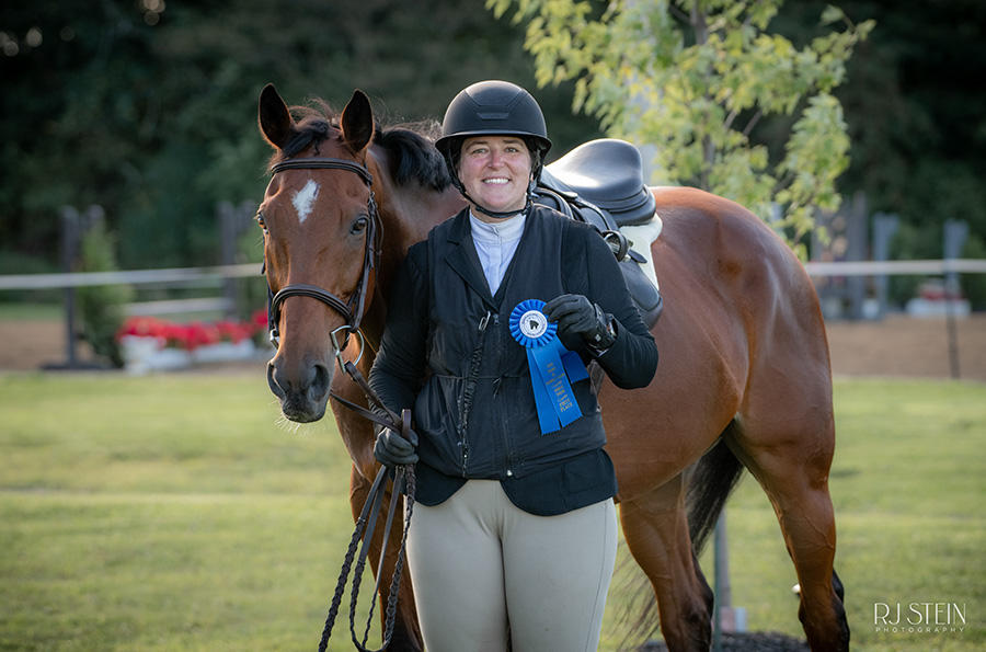 Women holding a blue ribbon while posing with her horse